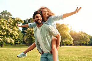 A couple playing in a park with the woman sitting on the man's shoulders