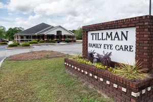 A brick sign for Tillman Family Eye Care in front of a building and plants