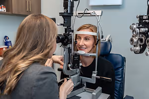 A woman sitting in an optometrist's chair having her eyes examined by another woman in a room