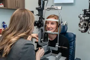 A woman sitting in an optometrist's chair having her eyes examined by another woman in a room