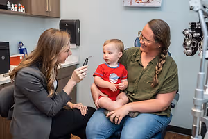 Two women are examining a child's eyes with a dental mirror inside an office room.