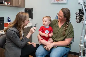 Two women are examining a child's eyes with a dental mirror inside an office room.