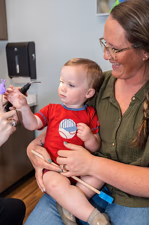 An adult female is holding a baby on her lap while the baby's teeth are being cleaned by a dentist.