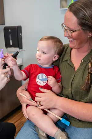 An adult female is holding a baby on her lap while the baby's teeth are being cleaned by a dentist.