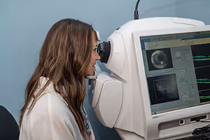 A young woman is having her eye examined by an optometrist using an optical coherence tomography machine.