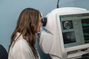 A young woman is having her eye examined by an optometrist using an optical coherence tomography machine.