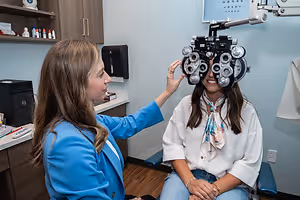 A young woman is getting her eyes checked by a doctor in a blue coat