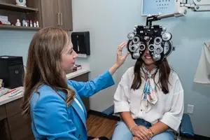 A young woman is getting her eyes checked by a doctor in a blue coat