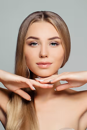 A woman is posing for a photo, with her hands on her neck and chin, and a serious expression on her face.
