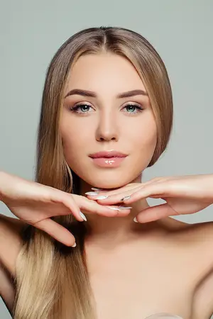 A woman is posing for a photo, with her hands on her neck and chin, and a serious expression on her face.