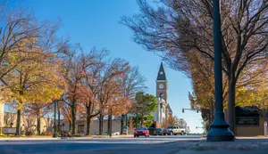 A Fort Smith AR town street with trees and a clock tower in the distance, with a red car parked on the side of the road