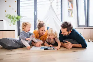 A family is sitting on the floor, reading a book together.
