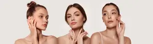Three women with bare shoulders are posing for a photograph with serious expressions, two of them touching their faces.