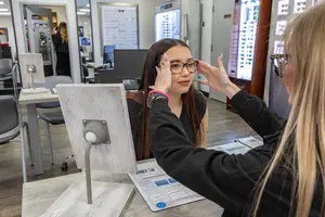 A woman is adjusting glasses on another woman in a vision care clinic