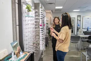 Two women standing in front of a shelf of eyeglasses in a shop