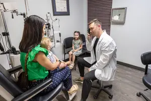 A man in a white lab coat examining a child's eyes in an eye clinic.