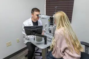 An adult man is examining a woman's eyes with a machine inside a clinic