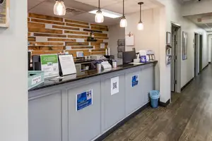 The interior of a waiting area with a wooden floor and a reception desk with a monitor, cups, and a trash bin.