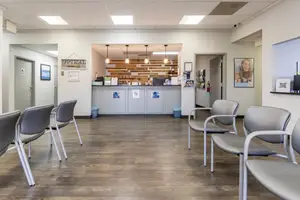 An empty waiting room with chairs, a reception desk, and wooden floor in a clinic or medical office.