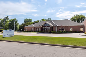 An exterior view of the Laster Eye Center in Oklahoma City, Oklahoma, with a sign, lush green lawn, brick walls, and trees in the distance under a blue sky with clouds.