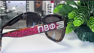 Brown sunglasses with a red rhinestone-studded side arm displayed in an optical store