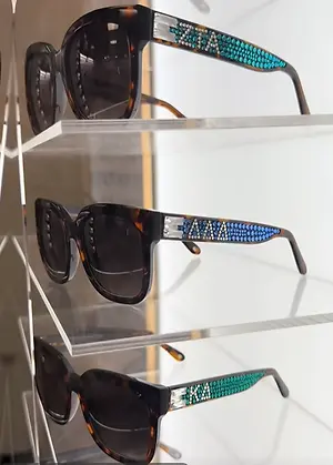 Three pairs of dark sunglasses with jeweled decorative frames displayed on clear shelves