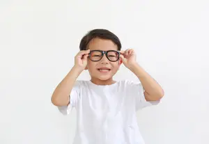 A smiling young boy wearing glasses and a white t-shirt.