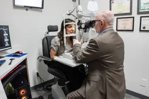 A man is examining a woman's eyes using an eye exam machine in a medical room.