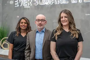 Three individuals posing for a picture in front of the Ever Square Eye sign