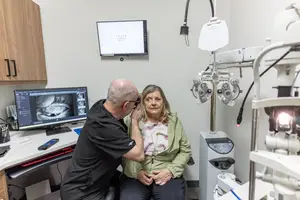 A man is checking a woman's eyes in a clinic room.