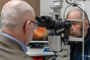Man looking through an eye examination machine while another man looks on
