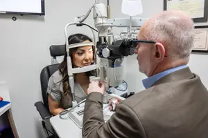 A man in a suit is examining a woman's eyes with a medical device