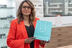 Woman with glasses holding a blue bag with the brand name on it