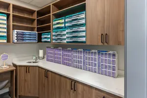 An office or study room with wooden cabinets and shelves with storage boxes and a white countertop with a sink, a bottle, and a tissue holder