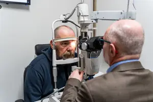 An eye specialist is examining a patient's eyes using an ophthalmoscope in a medical setting.