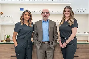 Three people standing in front of a glass display in an eyeglass shop