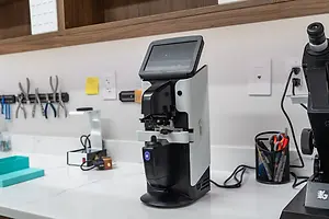 A microscope on a white countertop next to a black container of scissors and other items.