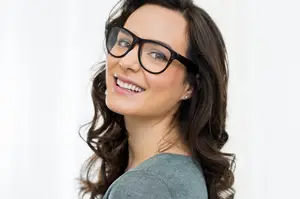 Close-up of a woman with curly brown hair, wearing black glasses, and smiling for the camera.