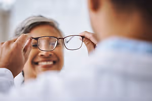 A woman trying on glasses with the help of a man wearing a white shirt