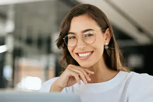 A woman with glasses and a white shirt is smiling and posing for a photo.