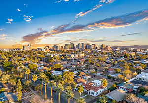 A view of a city at sunset with a blue sky and trees in the foreground