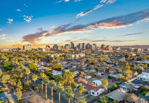 A view of a city at sunset with a blue sky and trees in the foreground