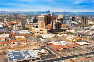 Aerial view of a city with many buildings, roads, and mountains in the distance under a blue sky