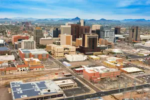 Aerial view of a city with many buildings, roads, and mountains in the distance under a blue sky