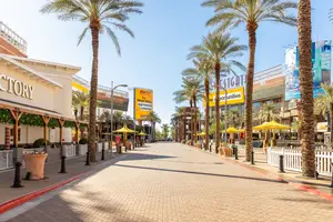 A quiet street with palm trees, shops, and umbrellas under a clear blue sky, perfect for a serene atmosphere.