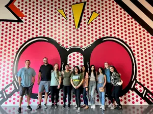 A group of people standing in front of a wall with a unique design of red dots and black lines.