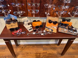 An indoor space that displays a wooden table with several pairs of glasses on it, and on top of the table is a book with a picture of a woman on it.