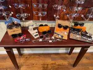 An indoor space that displays a wooden table with several pairs of glasses on it, and on top of the table is a book with a picture of a woman on it.