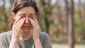 Image of a woman with her eyes closed and hands covering her face in a park setting