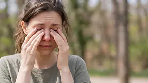 Image of a woman with her eyes closed and hands covering her face in a park setting